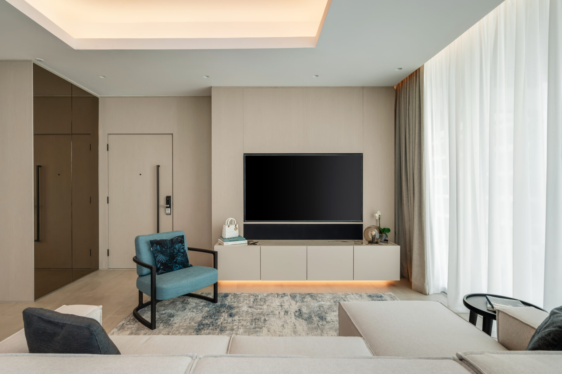 Front view of modern living room in Serenia Residences, Palm Jumeirah, with custom media wall, blue accent chair, and neutral sectional sofa.