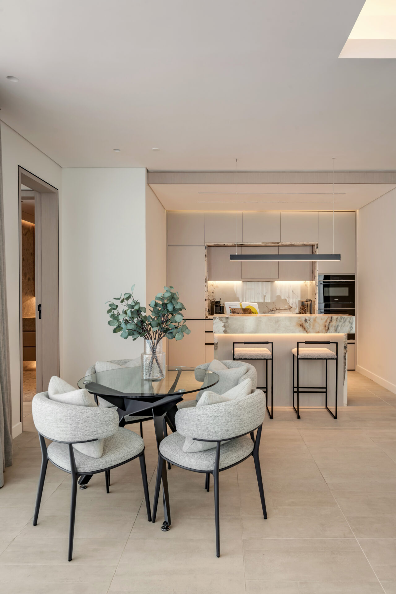 Open-plan dining and kitchen area in Serenia Residences, Palm Jumeirah, with round glass dining table, upholstered chairs, and marble breakfast bar.