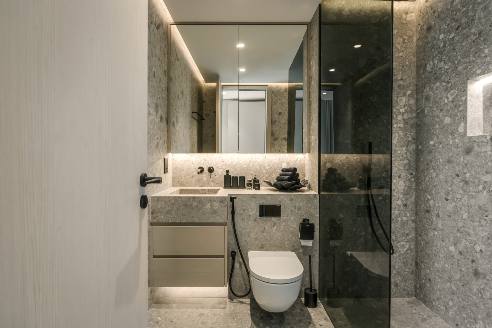 Modern bathroom with full-height grey terrazzo stone finishes, floating vanity, wall-mounted toilet, and glass-enclosed shower.