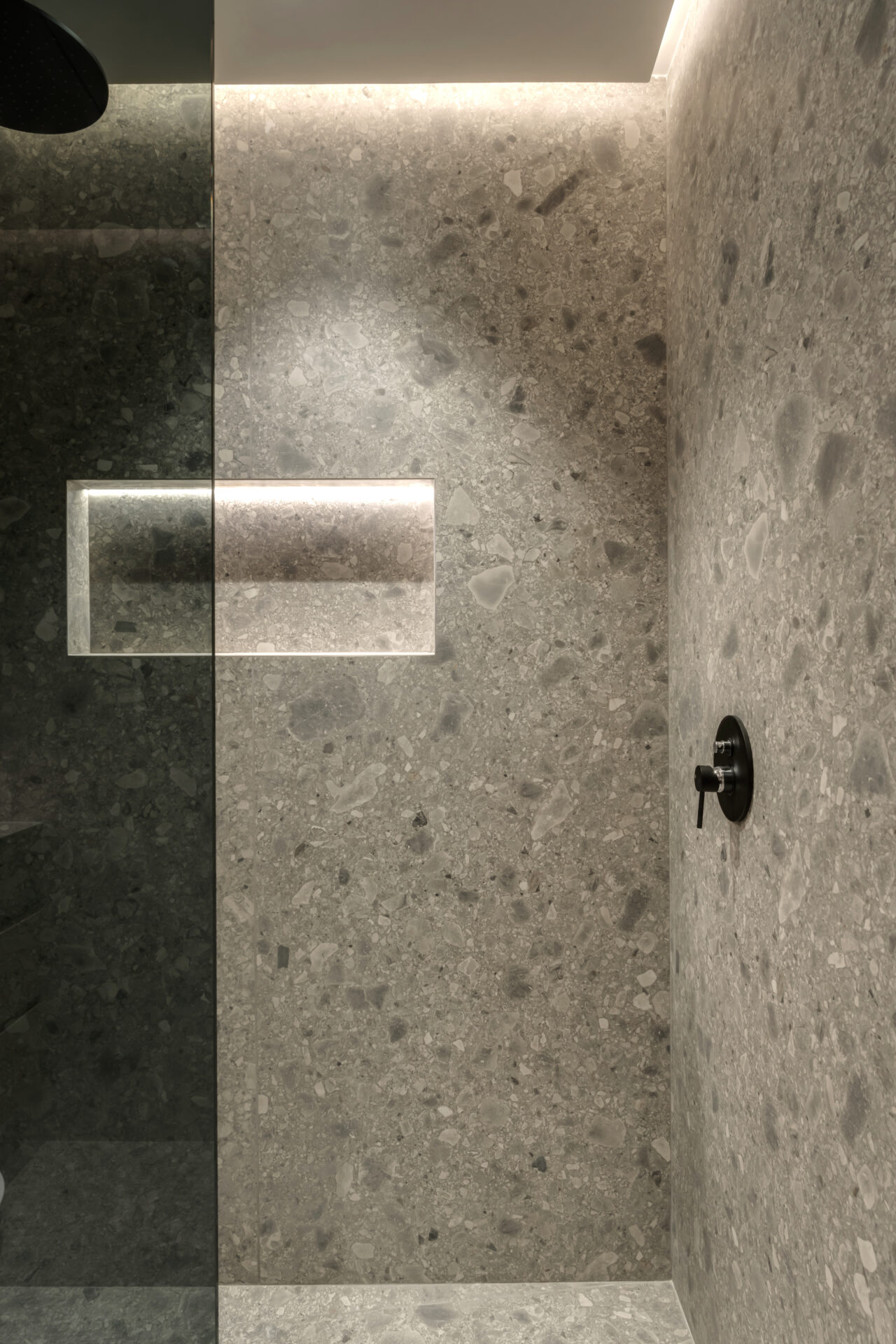 Modern shower with seamless grey Ceppo di Gré stone-effect tiling, built-in backlit niche, and matte black fixtures at Serenia Residences, Palm Jumeirah.