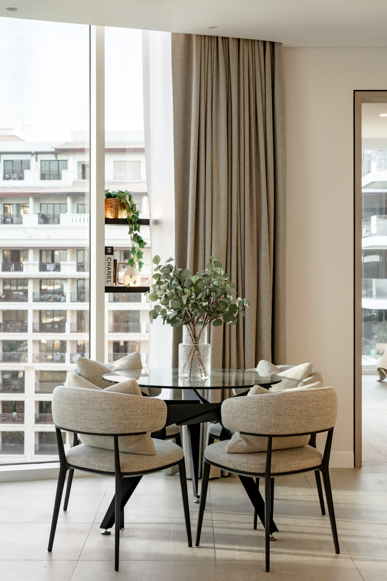 Modern round glass dining table with upholstered chairs and greenery centerpiece in a bright corner of a Serenia Residences apartment, Palm Jumeirah.