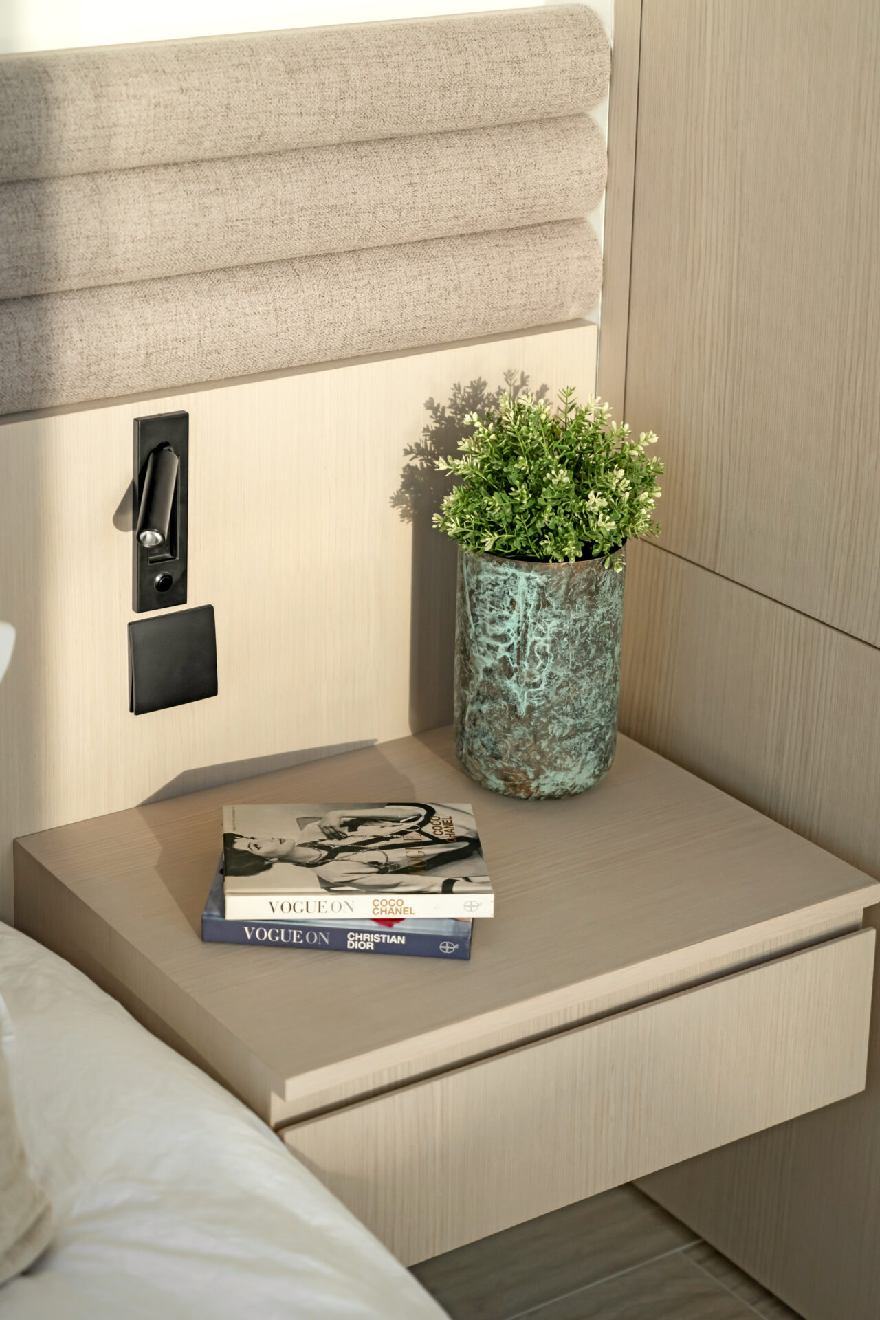 Close-up of a modern bedside table with books, potted plant, and integrated reading light.
