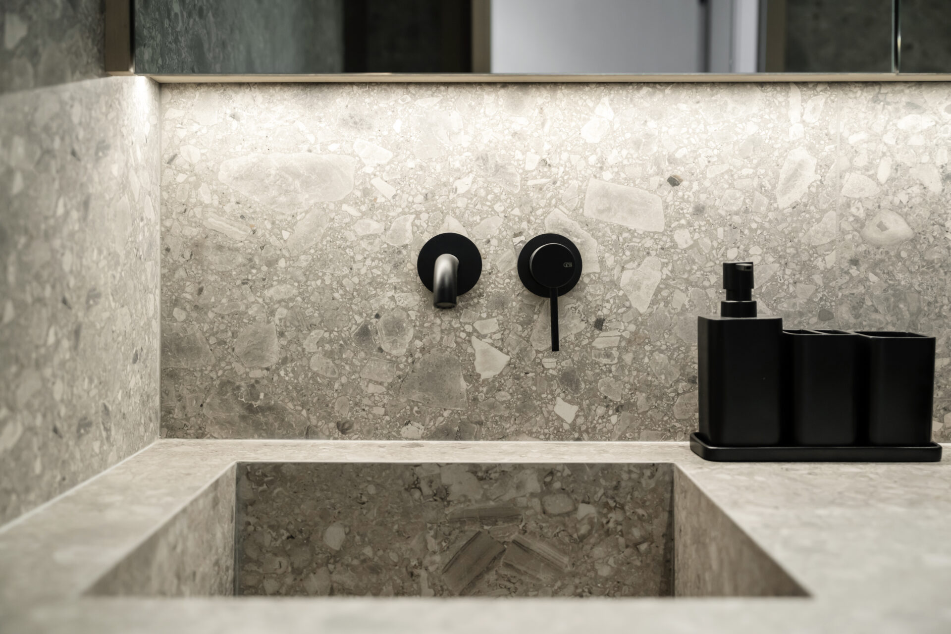Close-up of a terrazzo bathroom sink with matte black wall-mounted faucet and soap dispenser.