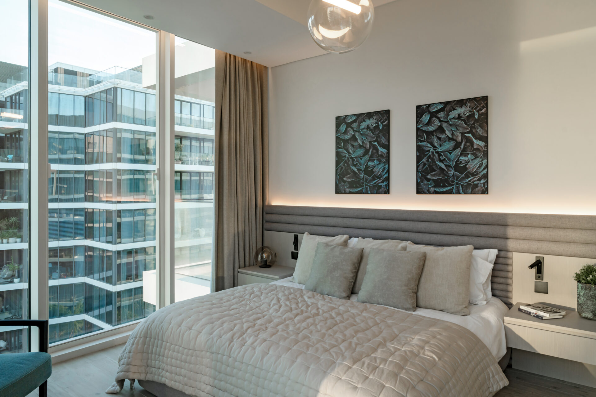 Modern bedroom in Serenia Residences, Palm Jumeirah, with full-width upholstered headboard, soft neutral bedding, and floor-to-ceiling windows overlooking contemporary architecture.