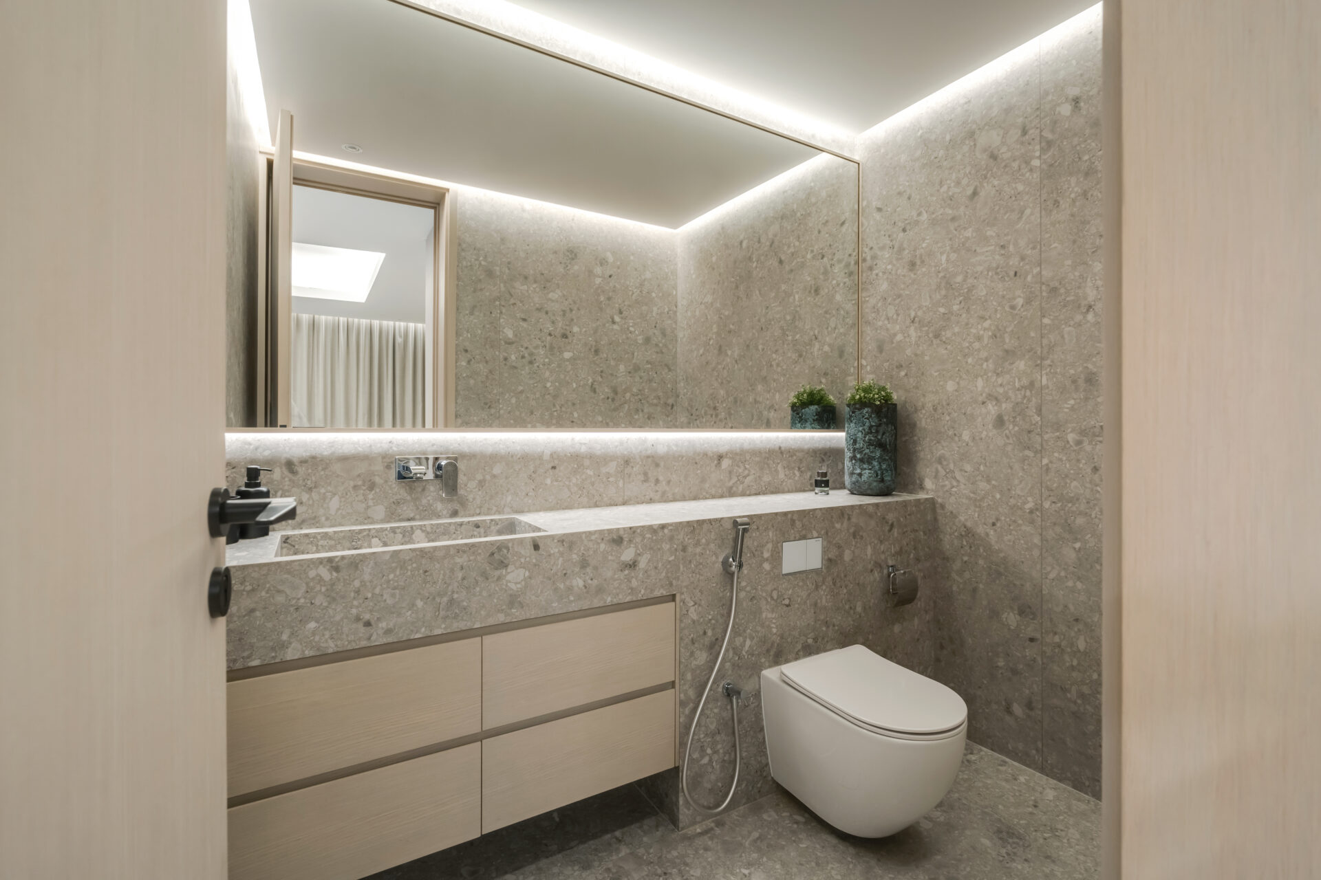 Modern powder room with seamless Ceppo di Gré stone-effect walls, integrated vanity, and concealed lighting in Serenia Residences, Palm Jumeirah.
