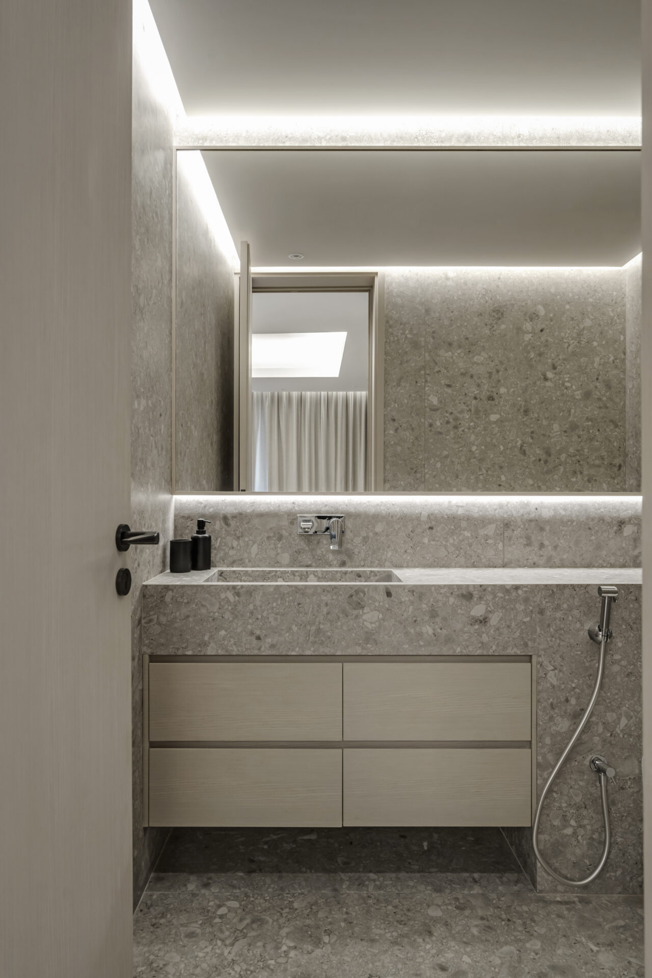 Minimalist bathroom with stone vanity, integrated mirror lighting, and light wood cabinetry.