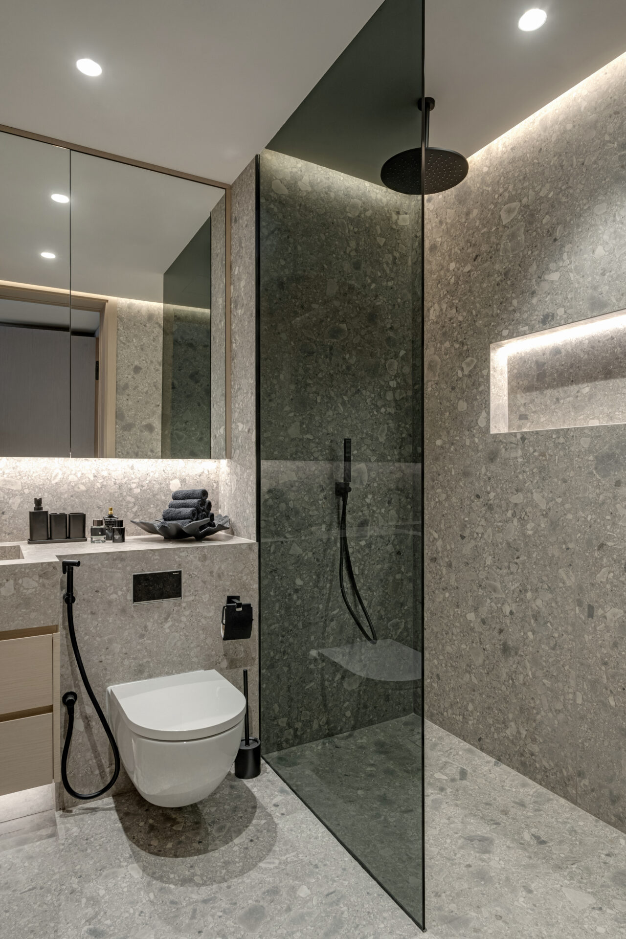 Contemporary bathroom with grey terrazzo stone, glass walk-in shower, wall-mounted toilet, and black fixtures.